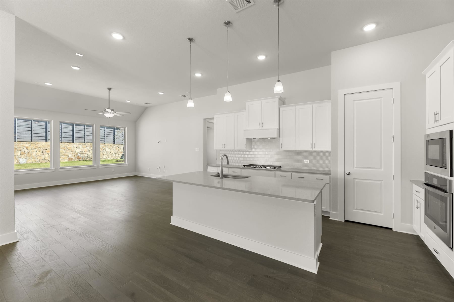 A modern, open-concept kitchen with white cabinets, stainless steel appliances, and dark hardwood floors, surrounded by large windows that allow natural light to fill the space.