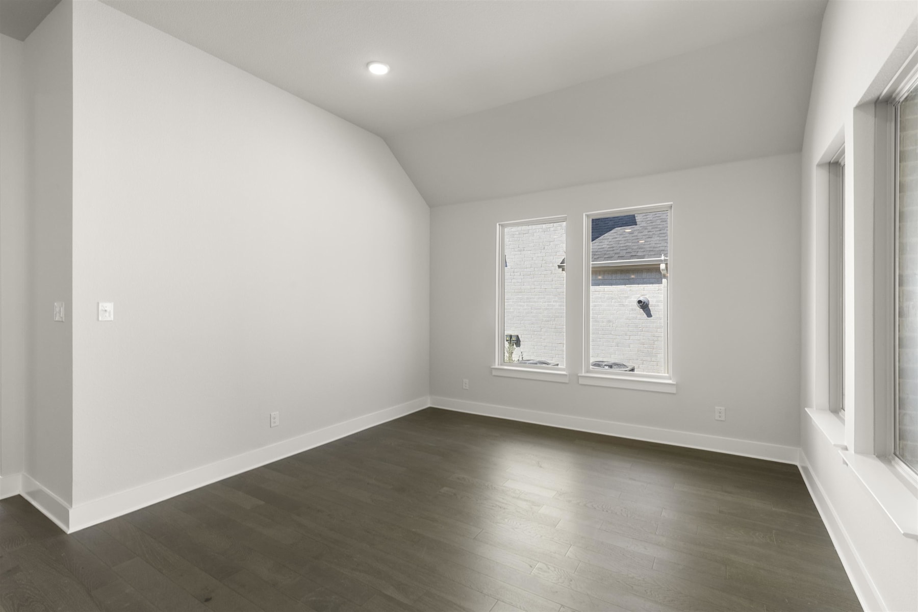 A minimalist, empty room with white walls, a single window, and dark hardwood flooring.