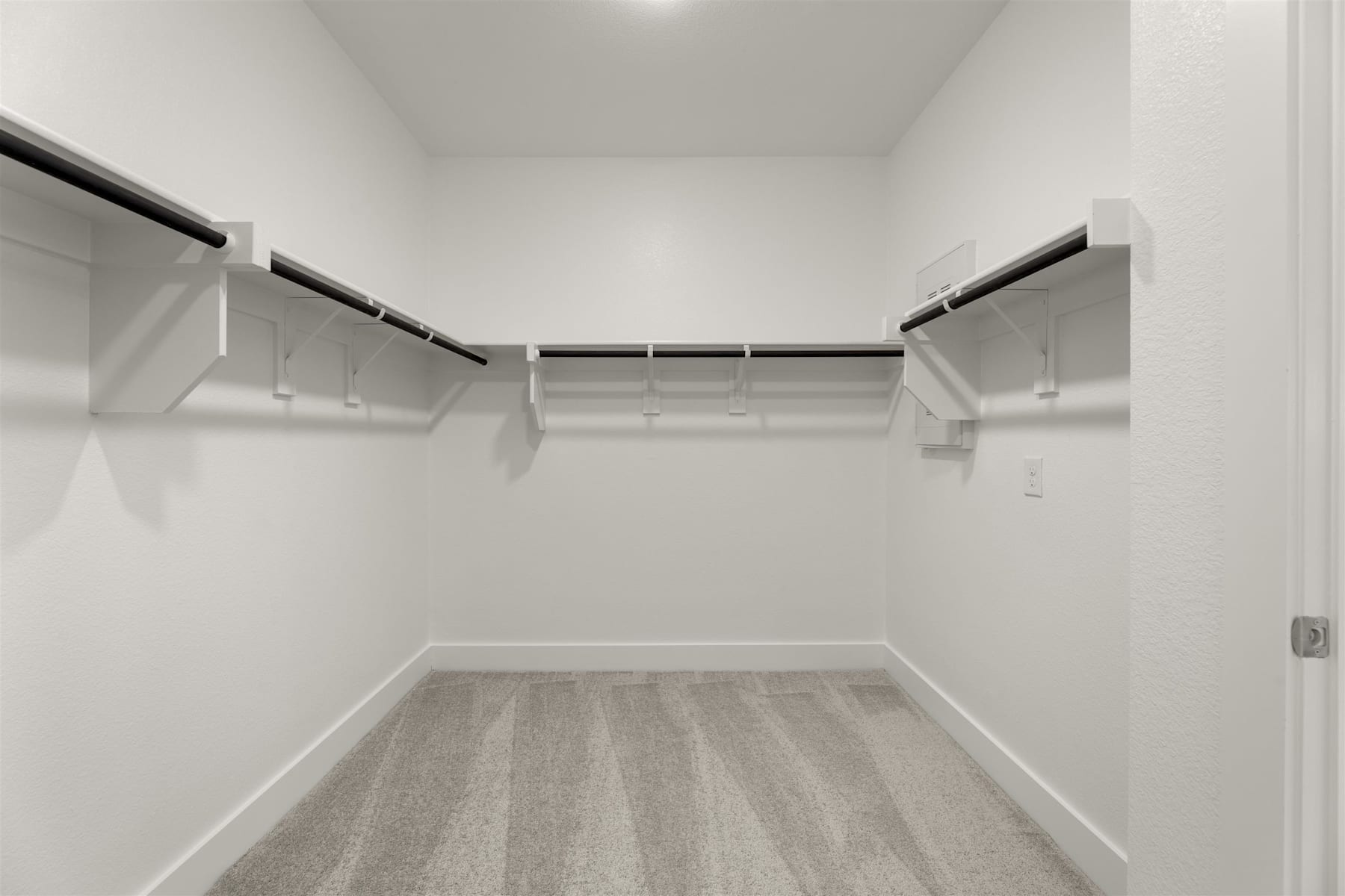A spacious, well-lit walk-in closet with white walls, wooden flooring, and multiple hanging rods for storing clothes.