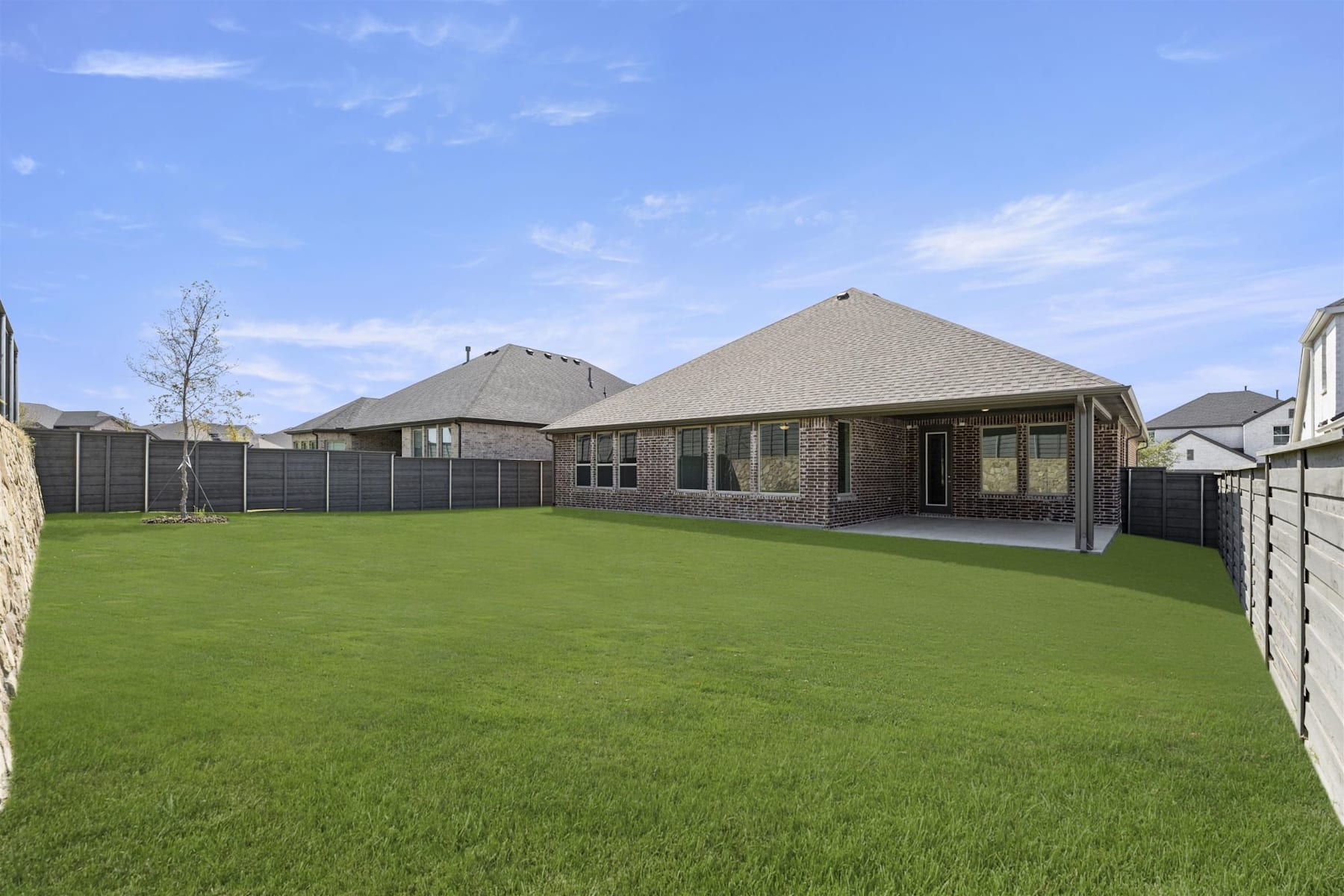 A well-manicured lawn stretches out in the foreground, leading to a large, brick-and-stone house with a peaked roof and a covered porch in the background.