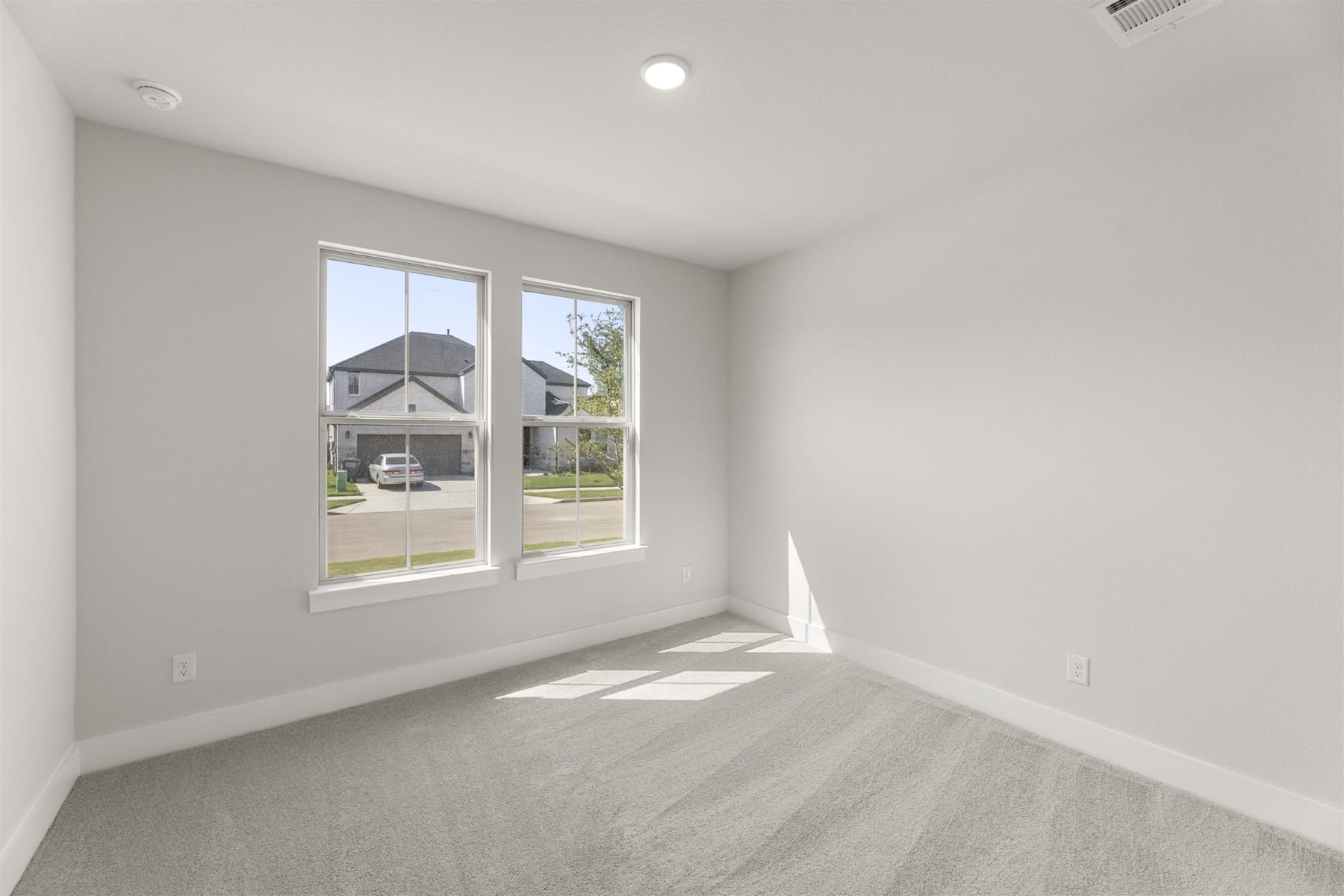 An empty, bright room with large windows overlooking a residential neighborhood outside.