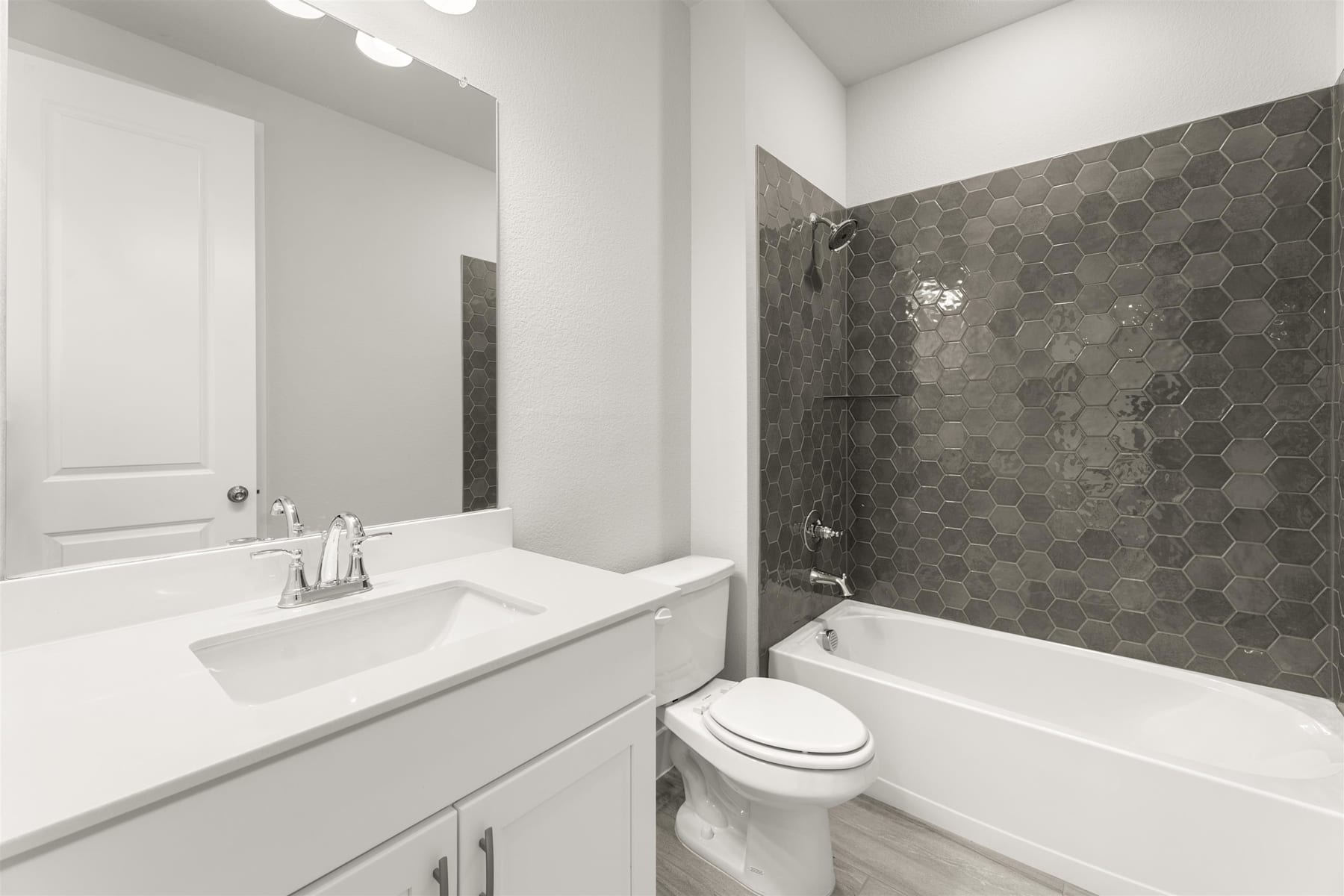 A modern bathroom with a white vanity, a bathtub, and a tiled wall with a hexagonal pattern.