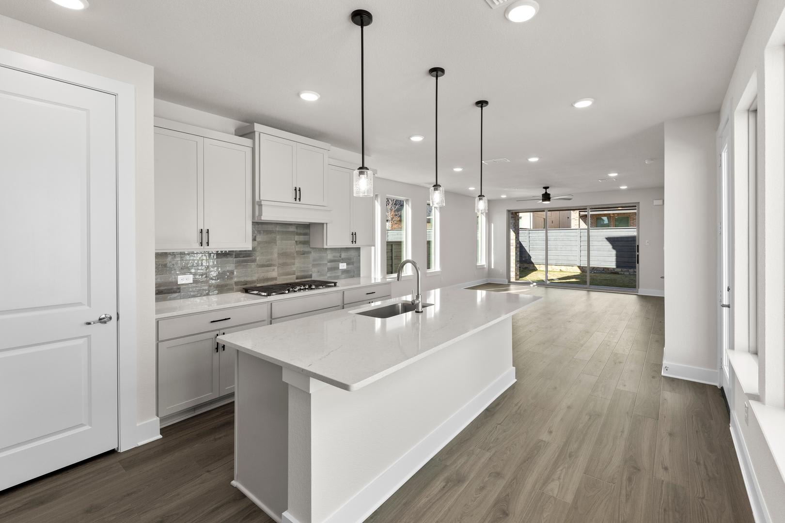 A modern, open-concept kitchen with white cabinets, a large island, and pendant lighting, leading into a spacious living area with hardwood floors.