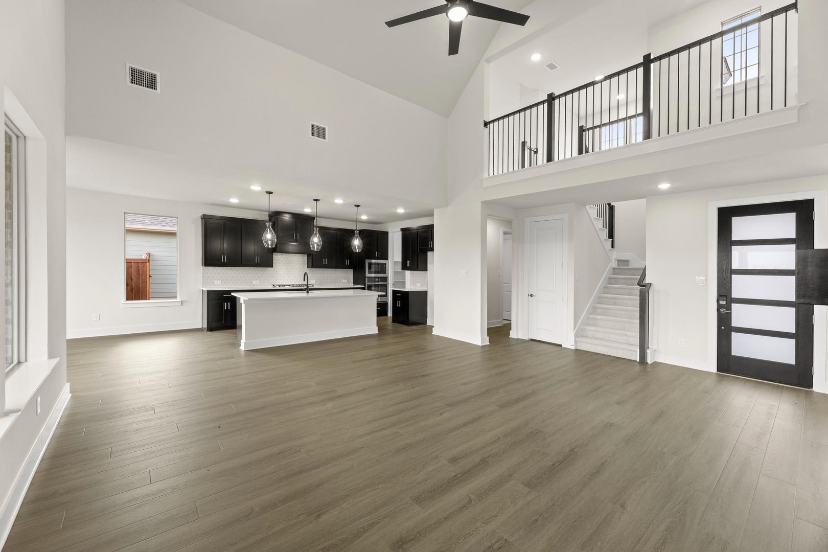 A modern, open-concept living space with a kitchen, hardwood floors, and a staircase leading to an upper level.