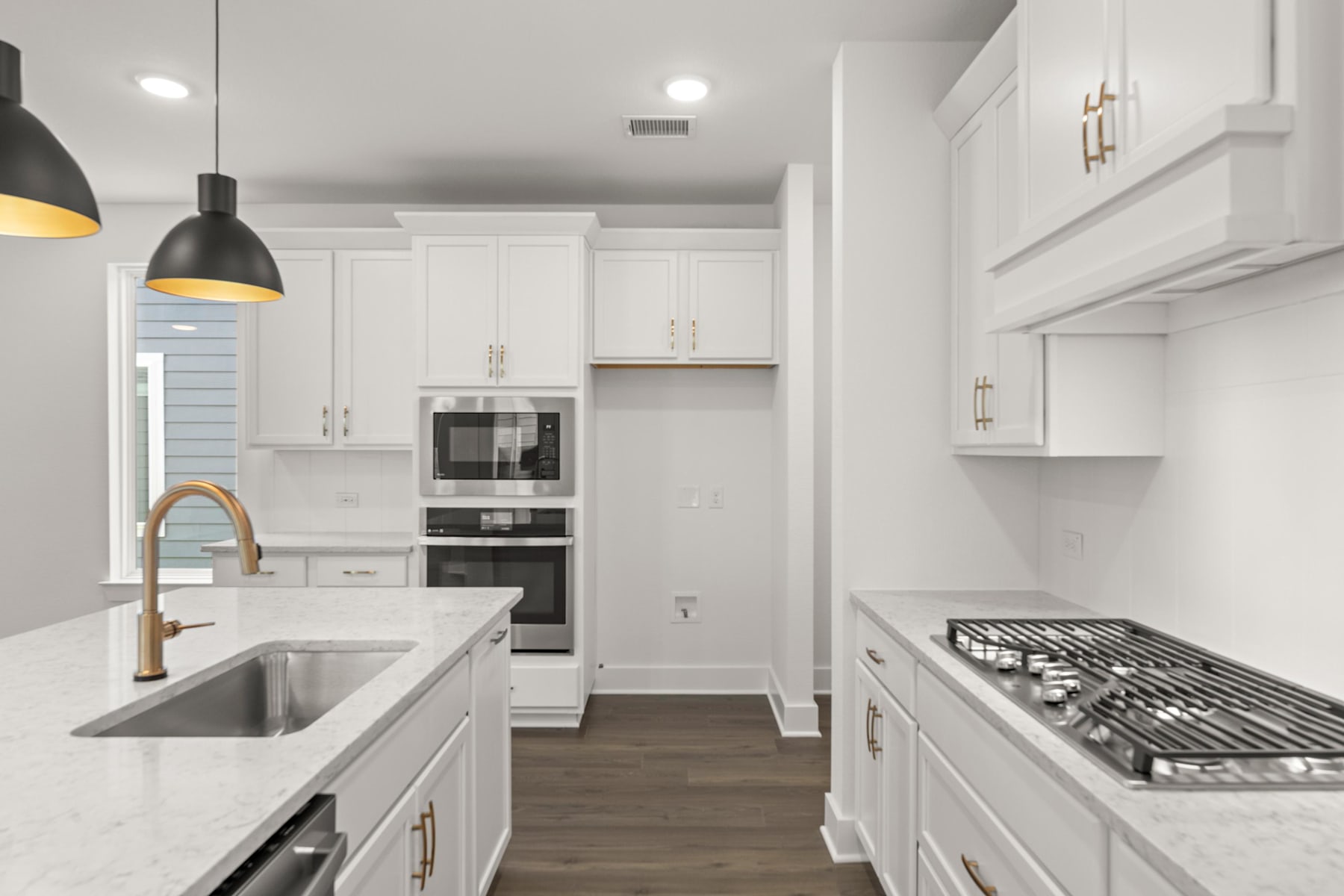 A modern, white kitchen with stainless steel appliances, wooden floors, and pendant lighting fixtures.