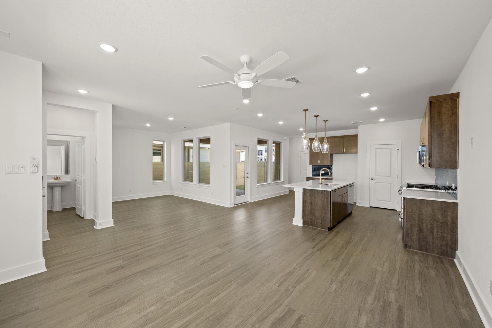 A spacious and well-lit open-concept living area with a kitchen island, hardwood floors, and a ceiling fan.