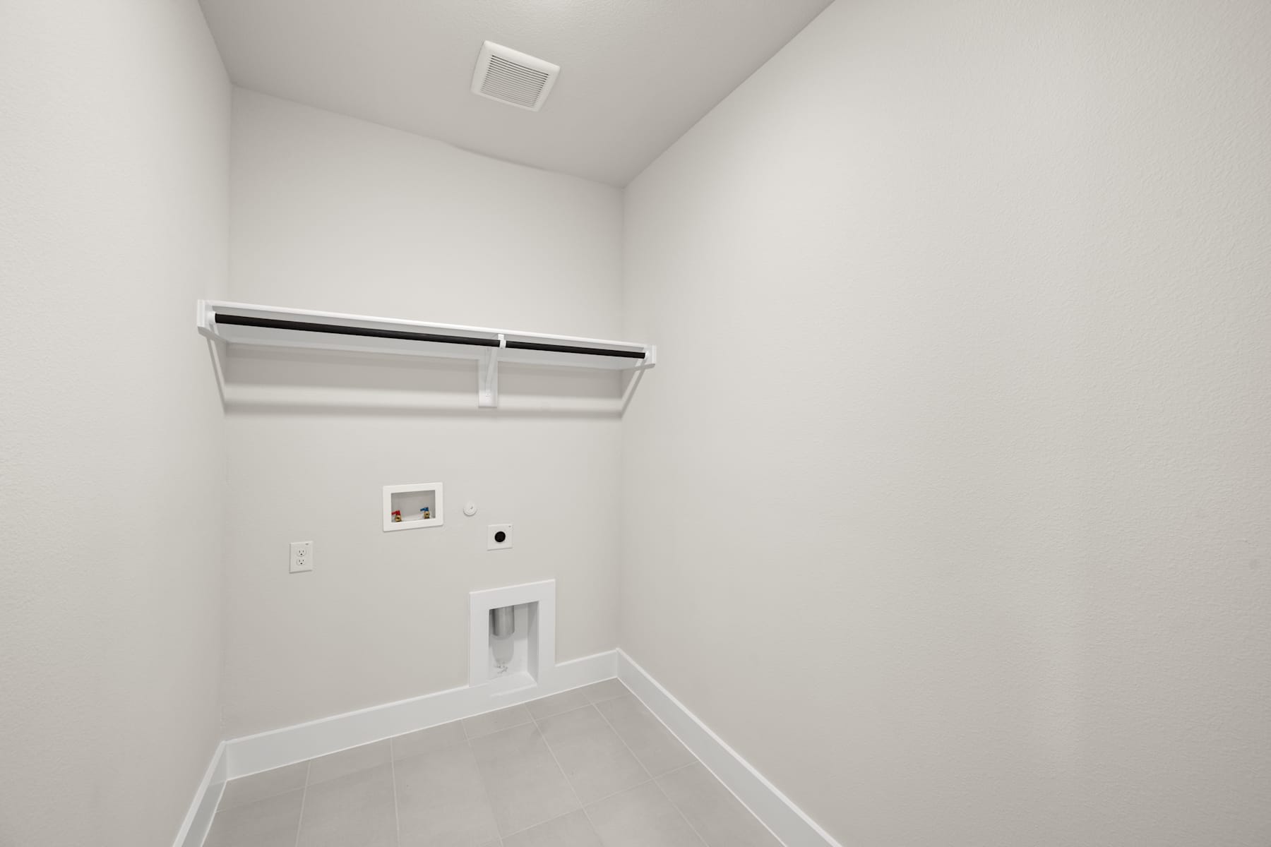 A small, empty room with white walls, a ceiling light fixture, and a shelf or storage unit mounted on the wall.