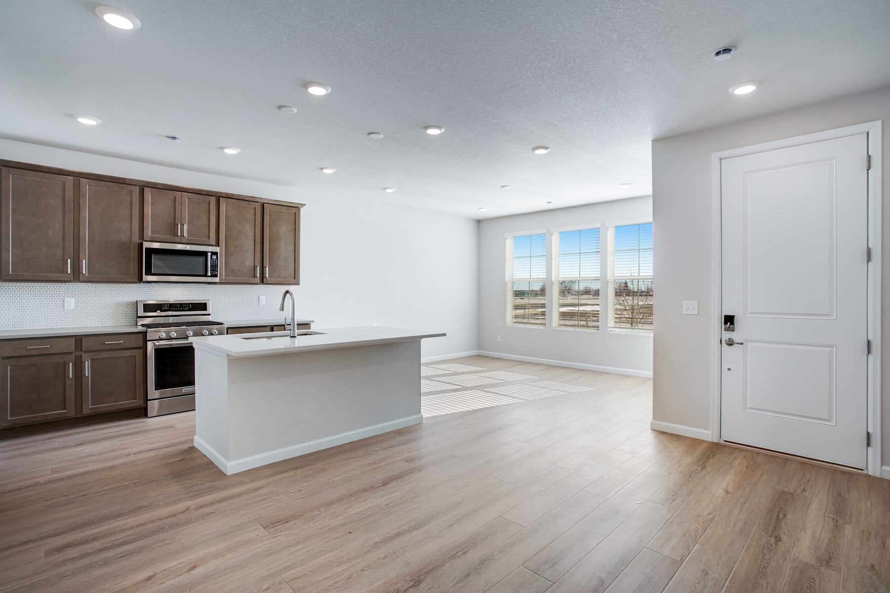 A modern, open-concept kitchen with dark wood cabinets, stainless steel appliances, and a white island countertop, set against a backdrop of large windows overlooking a scenic outdoor view.
