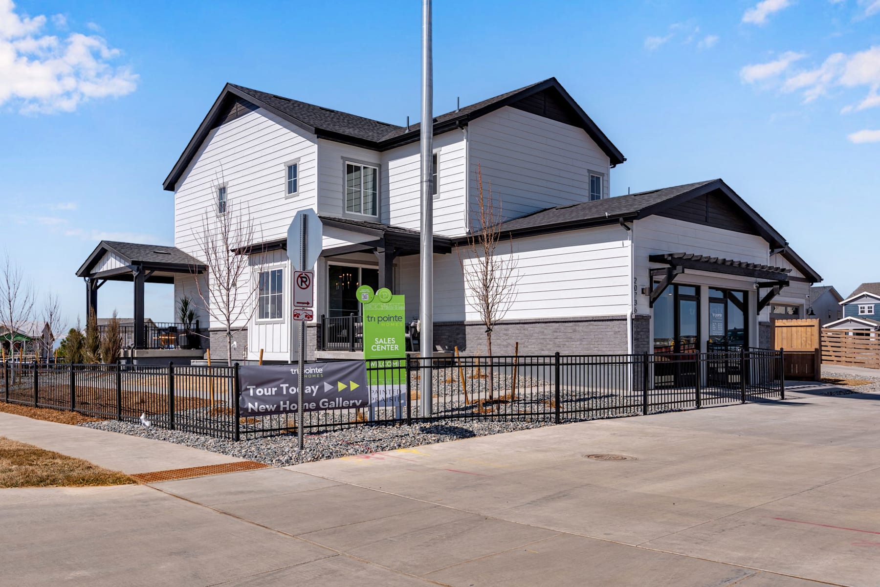 A two-story residential building with a porch and a fenced-in yard, set against a clear blue sky with scattered clouds.
