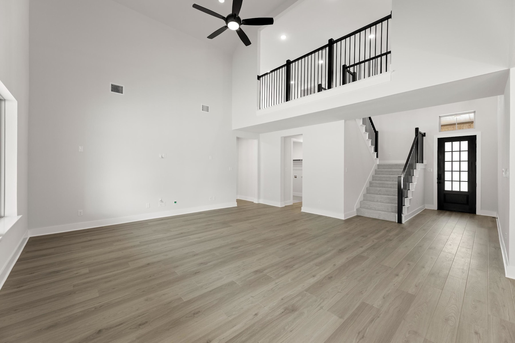 A spacious, open-concept interior with a high ceiling, hardwood floors, and a staircase leading to an upper level. The room features a ceiling fan and a large window, creating a bright and airy atmosphere.