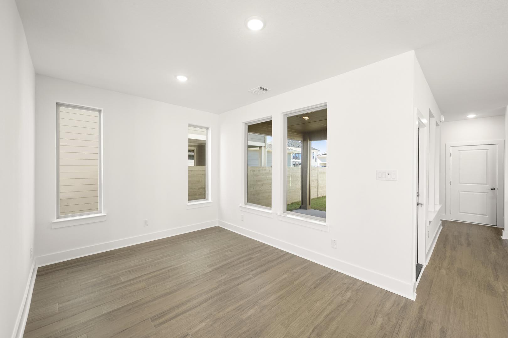 A bright, spacious room with white walls, hardwood floors, and large windows that let in natural light.