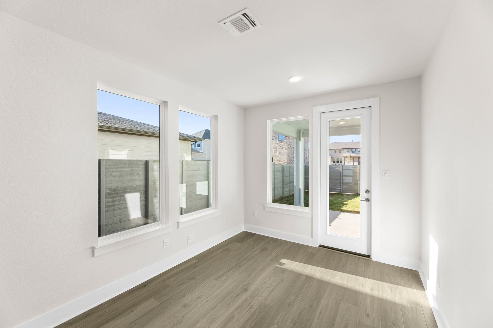 A bright and spacious room with white walls, a wooden floor, and large windows that allow natural light to flood the space.