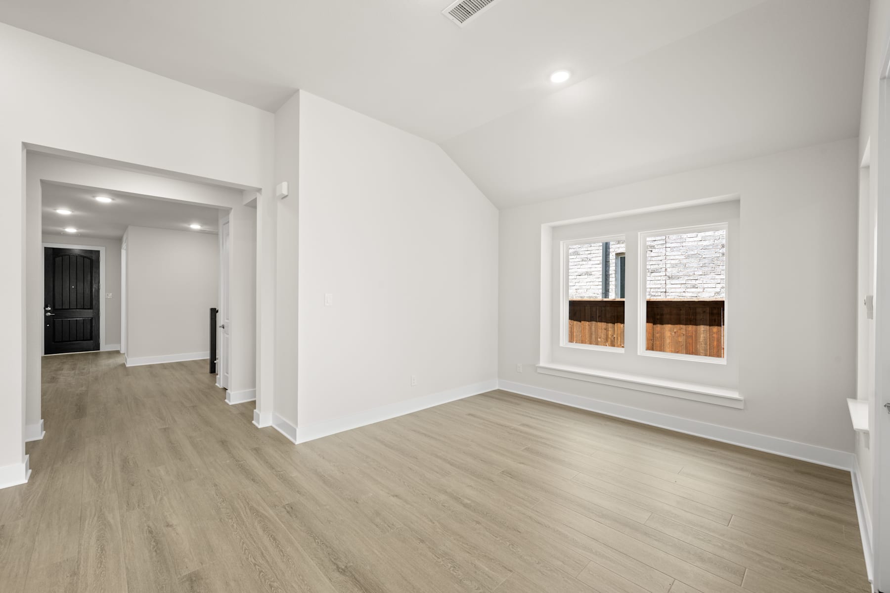 A spacious, well-lit room with white walls, a wooden floor, and a window providing natural light.