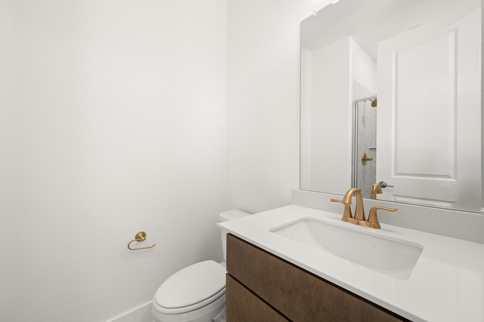 A modern, minimalist bathroom with a white vanity, a mirror, and a toilet in the background.