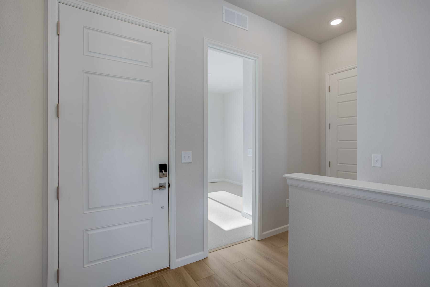A bright, minimalist hallway with white doors, a mirror, and hardwood flooring.