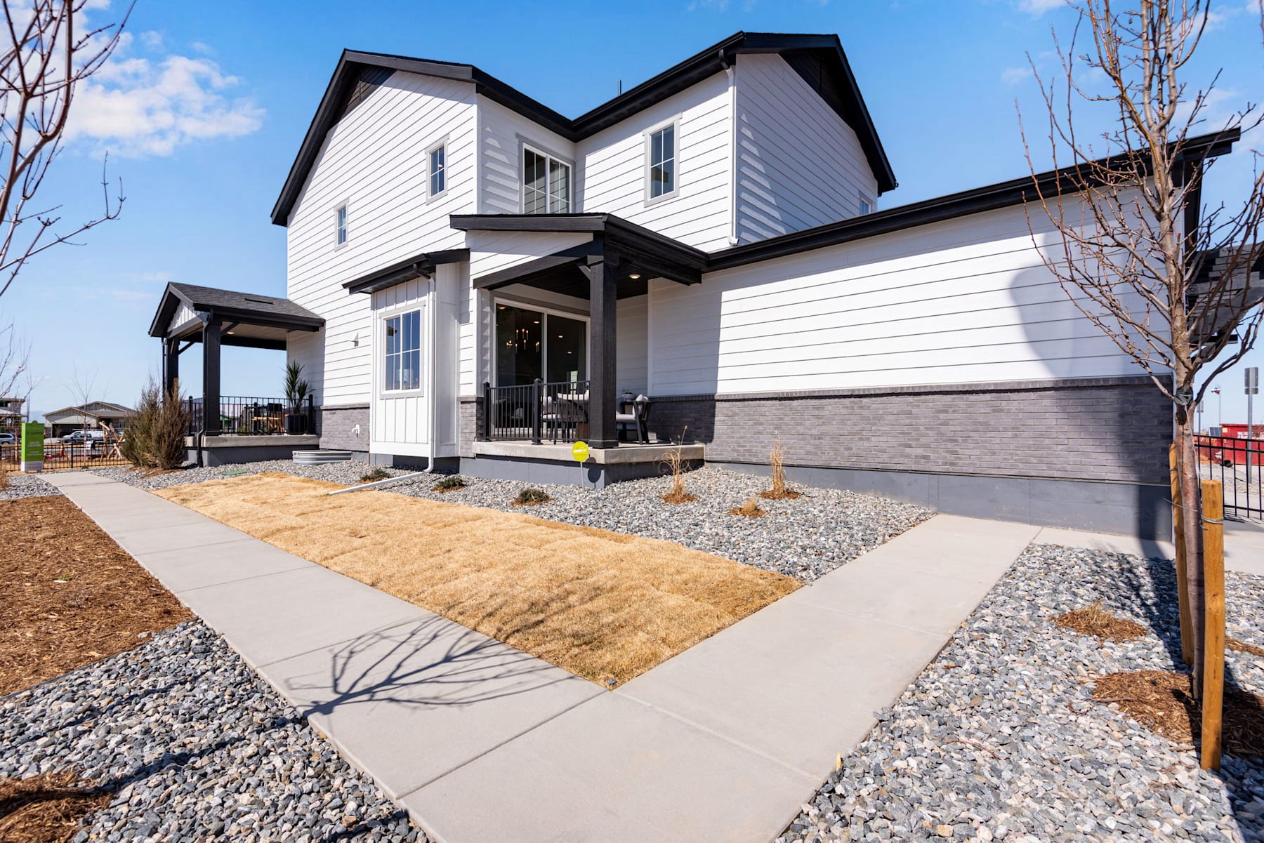 A modern, two-story white house with a covered porch and a gravel driveway leading up to it, set against a backdrop of blue sky and bare trees.