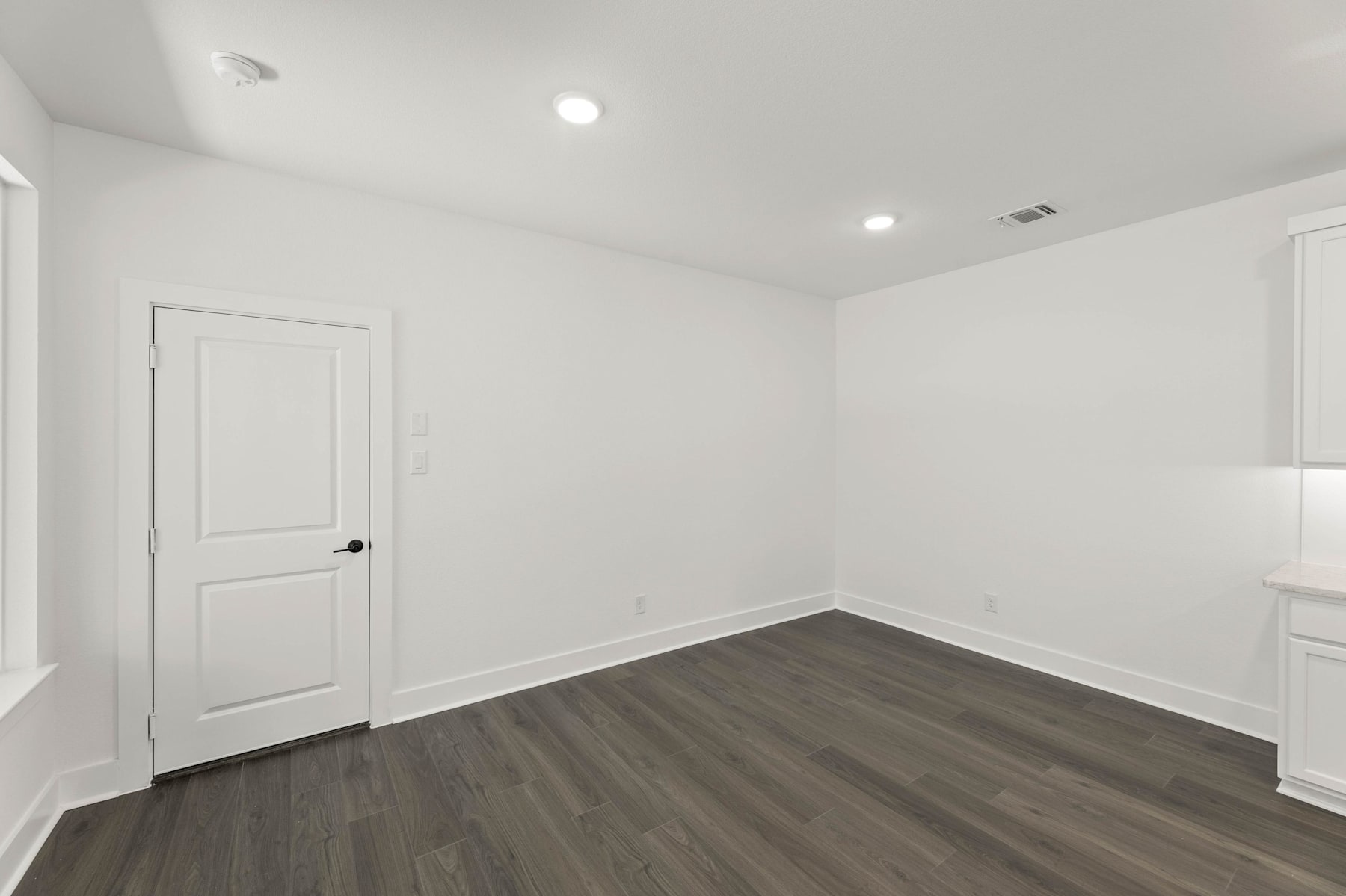 A simple, minimalist room with white walls, a dark hardwood floor, and a single white door.