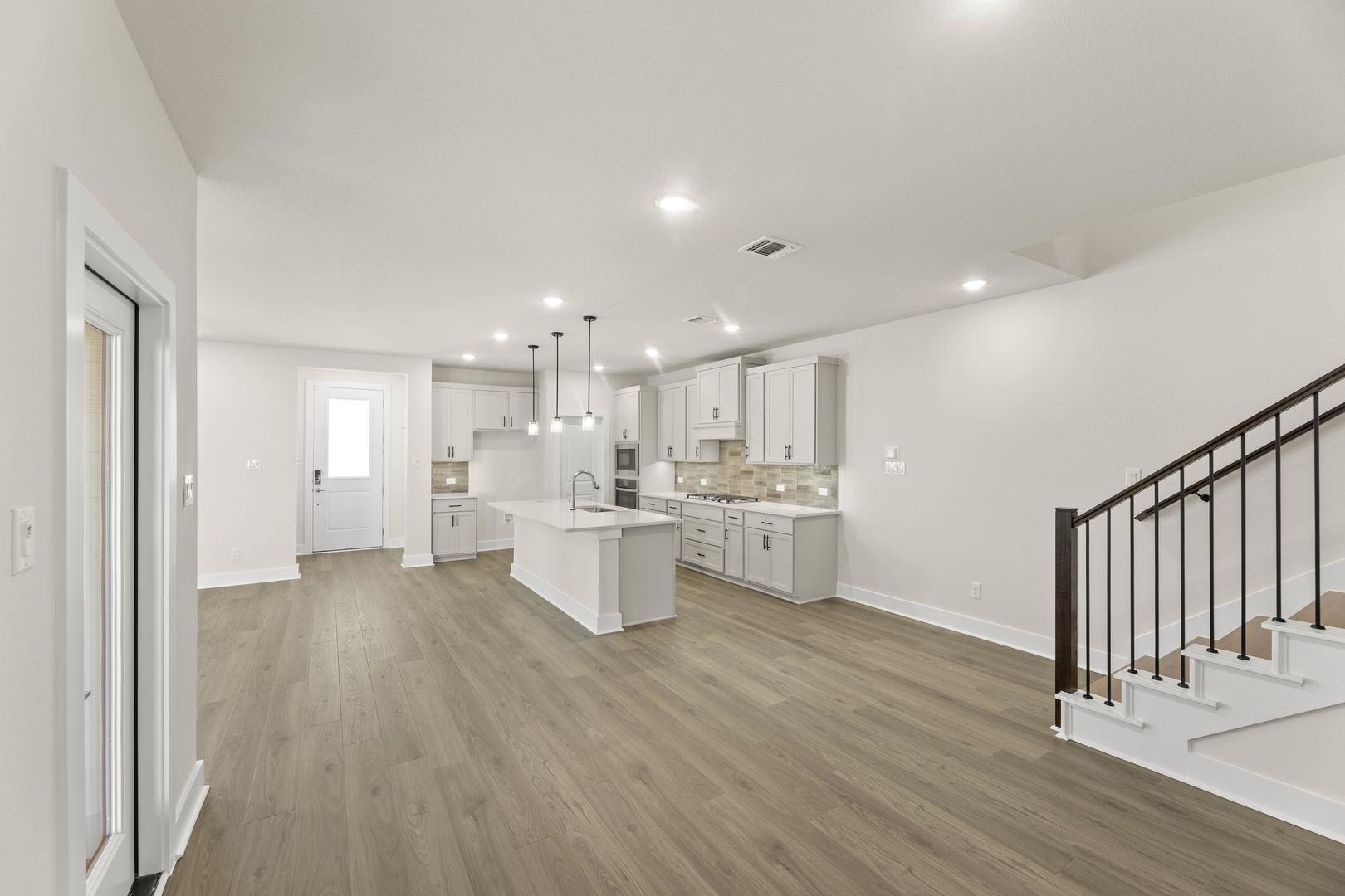 A spacious and modern kitchen with white cabinets, hardwood floors, and a staircase leading to the upper level.