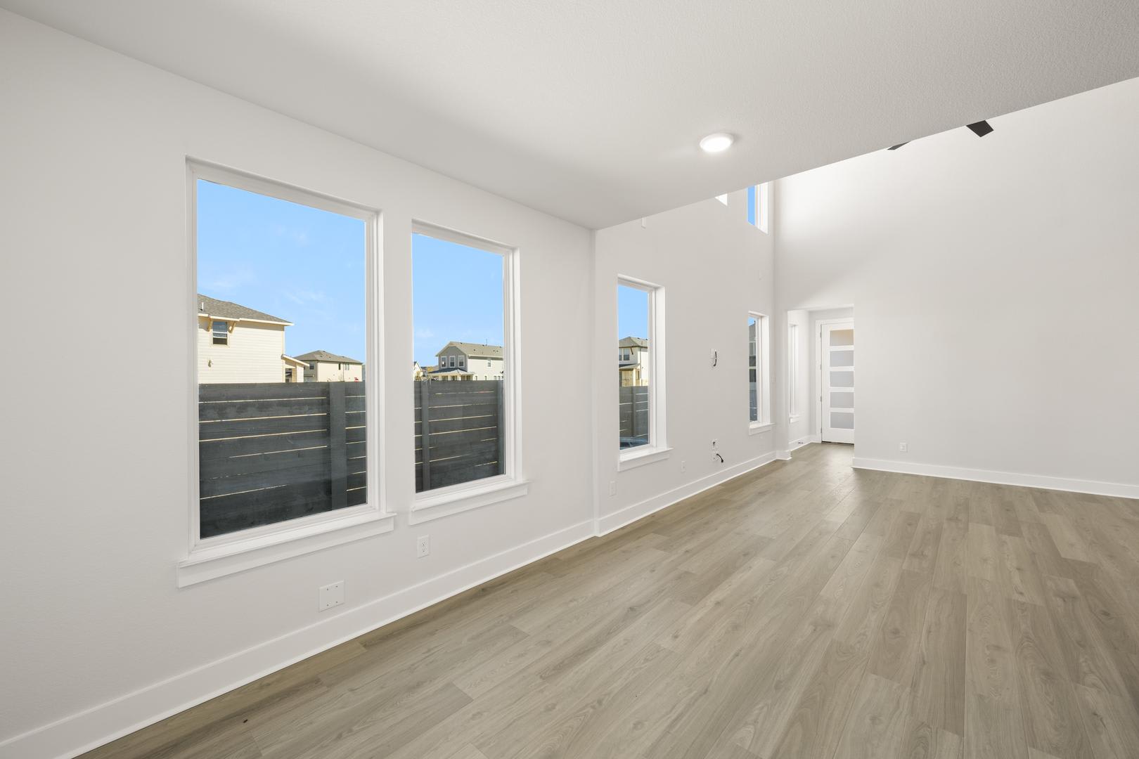 A bright, spacious room with large windows overlooking a residential neighborhood, featuring a hardwood floor and clean, minimalist decor.