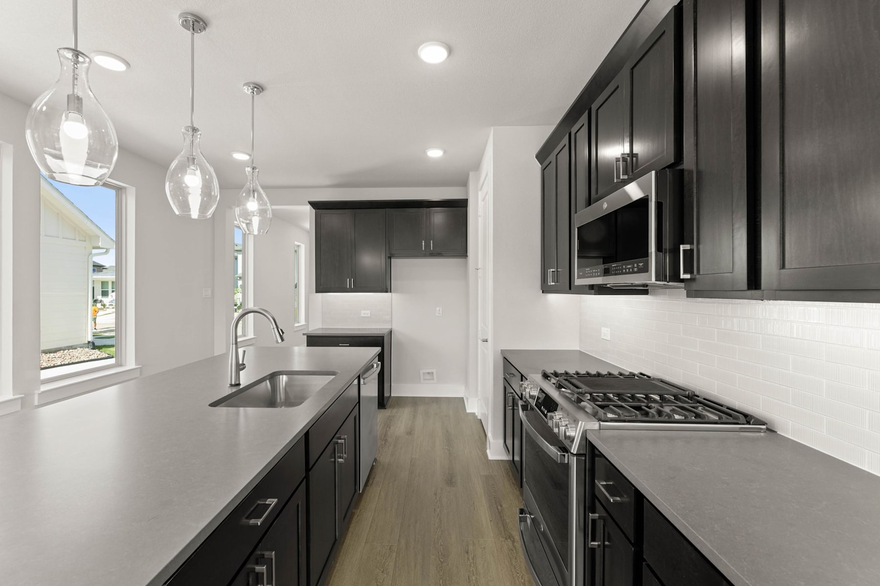 A modern, sleek kitchen with dark cabinets, stainless steel appliances, and pendant lighting fixtures, set against a bright and airy background.