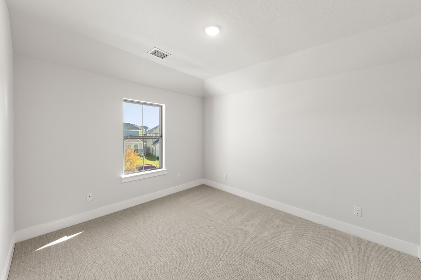 A bright, empty room with a window overlooking a yard in the background.