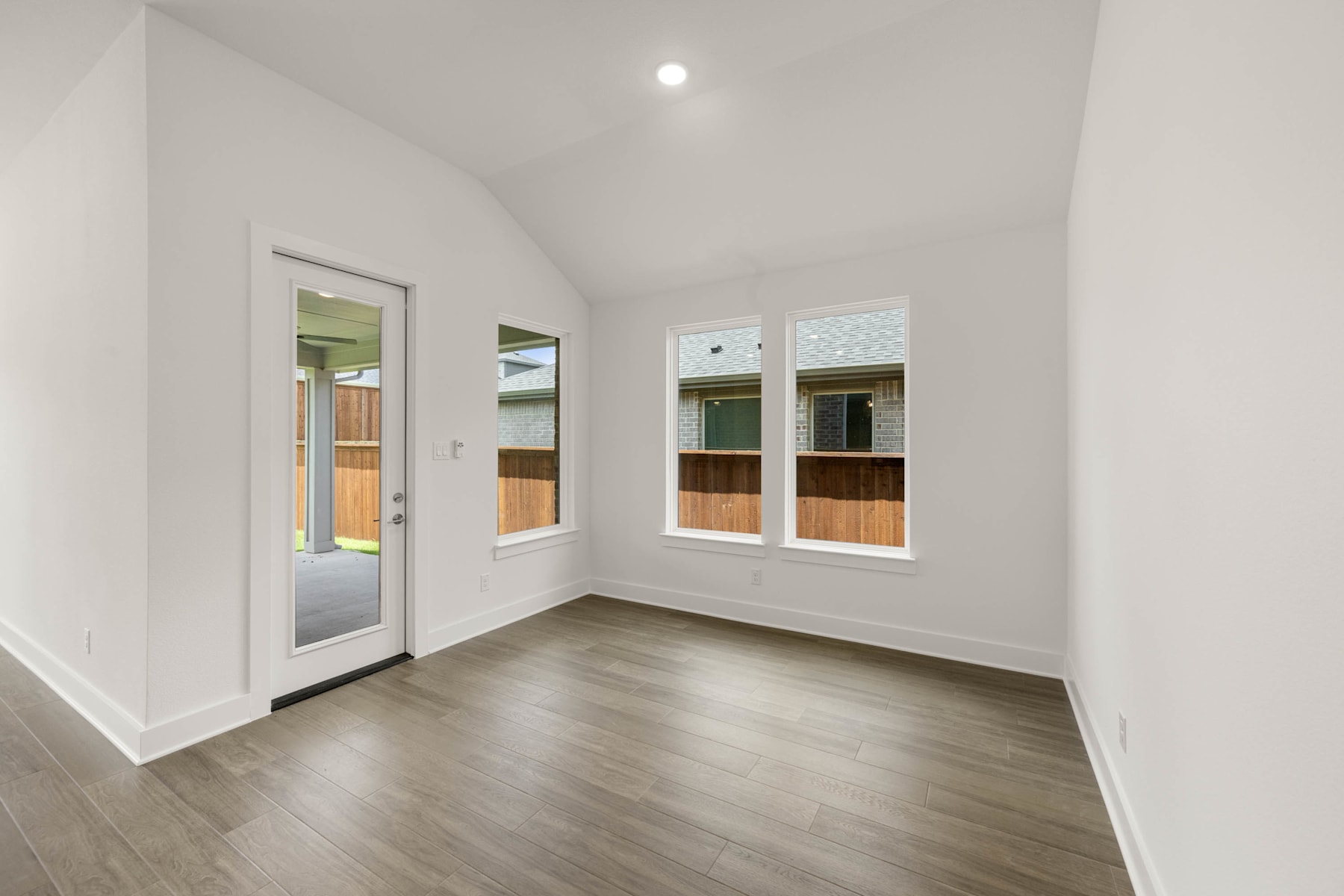A bright, minimalist room with white walls, a wooden floor, and large windows providing natural light.