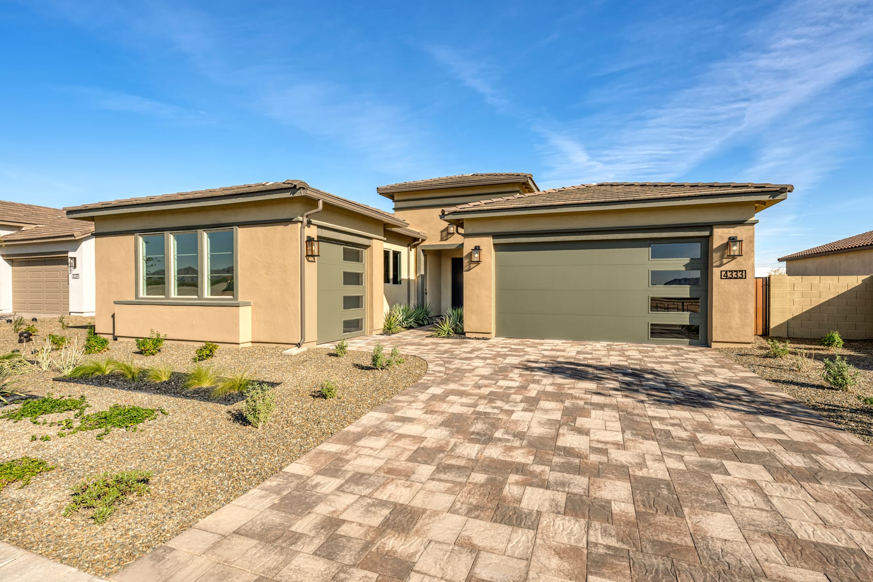 A modern, single-story house with a paved driveway and landscaped yard set against a clear blue sky with wispy clouds.