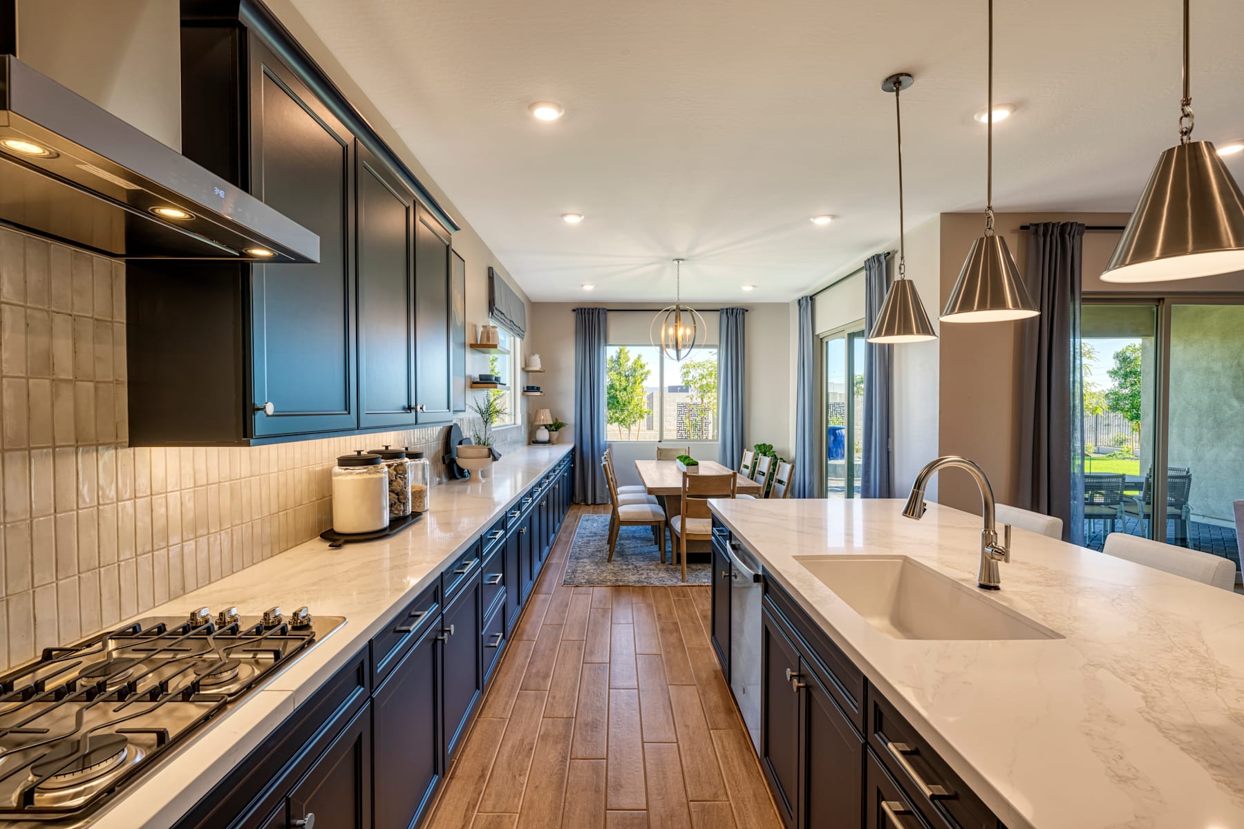 A modern and spacious kitchen with dark blue cabinets, a large central island, and pendant lighting fixtures, set against a backdrop of large windows overlooking a scenic outdoor view.