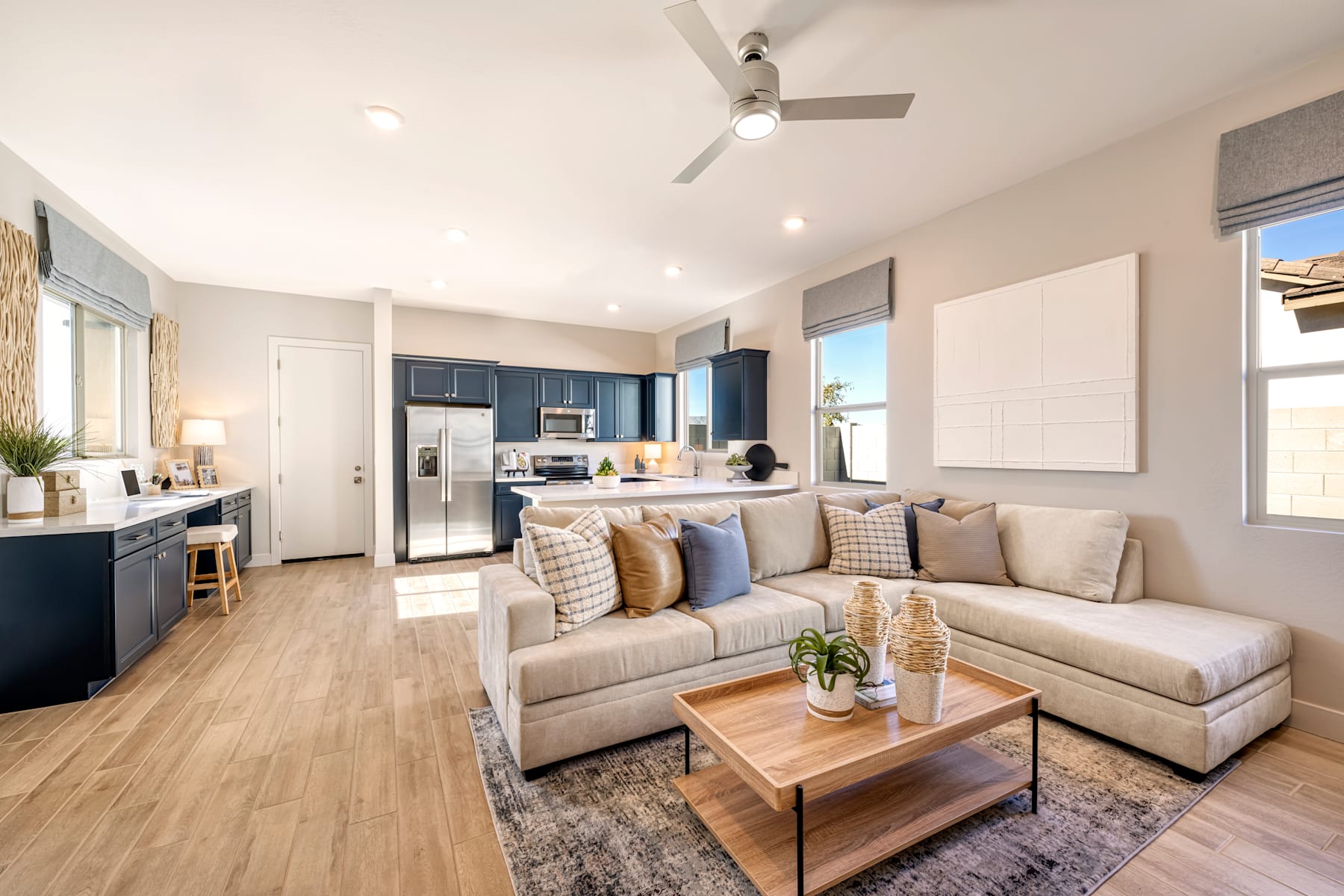 A modern and cozy living room with a comfortable sectional sofa, a wooden coffee table, and a kitchen visible in the background with stainless steel appliances.