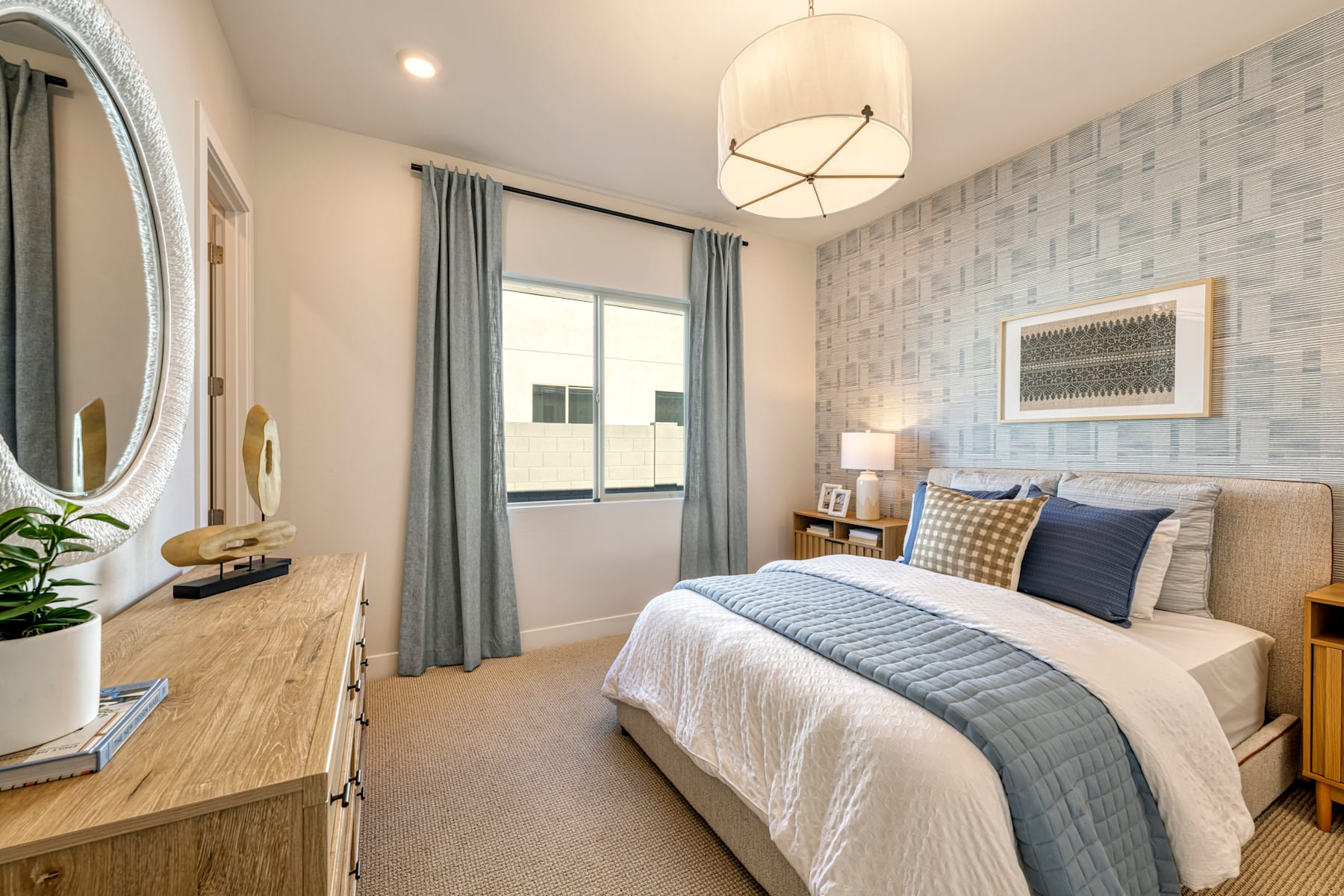 A cozy and well-designed bedroom with a large bed, a dresser, and a decorative mirror on the wall, complemented by a patterned accent wall and curtains.