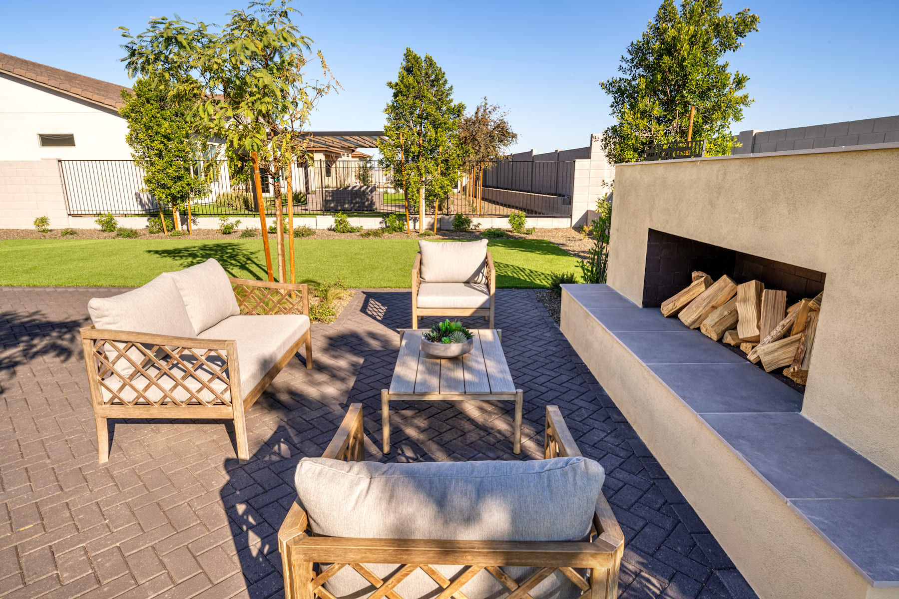 A cozy outdoor seating area with wooden furniture and a well-maintained lawn surrounded by trees and a brick wall in the background.