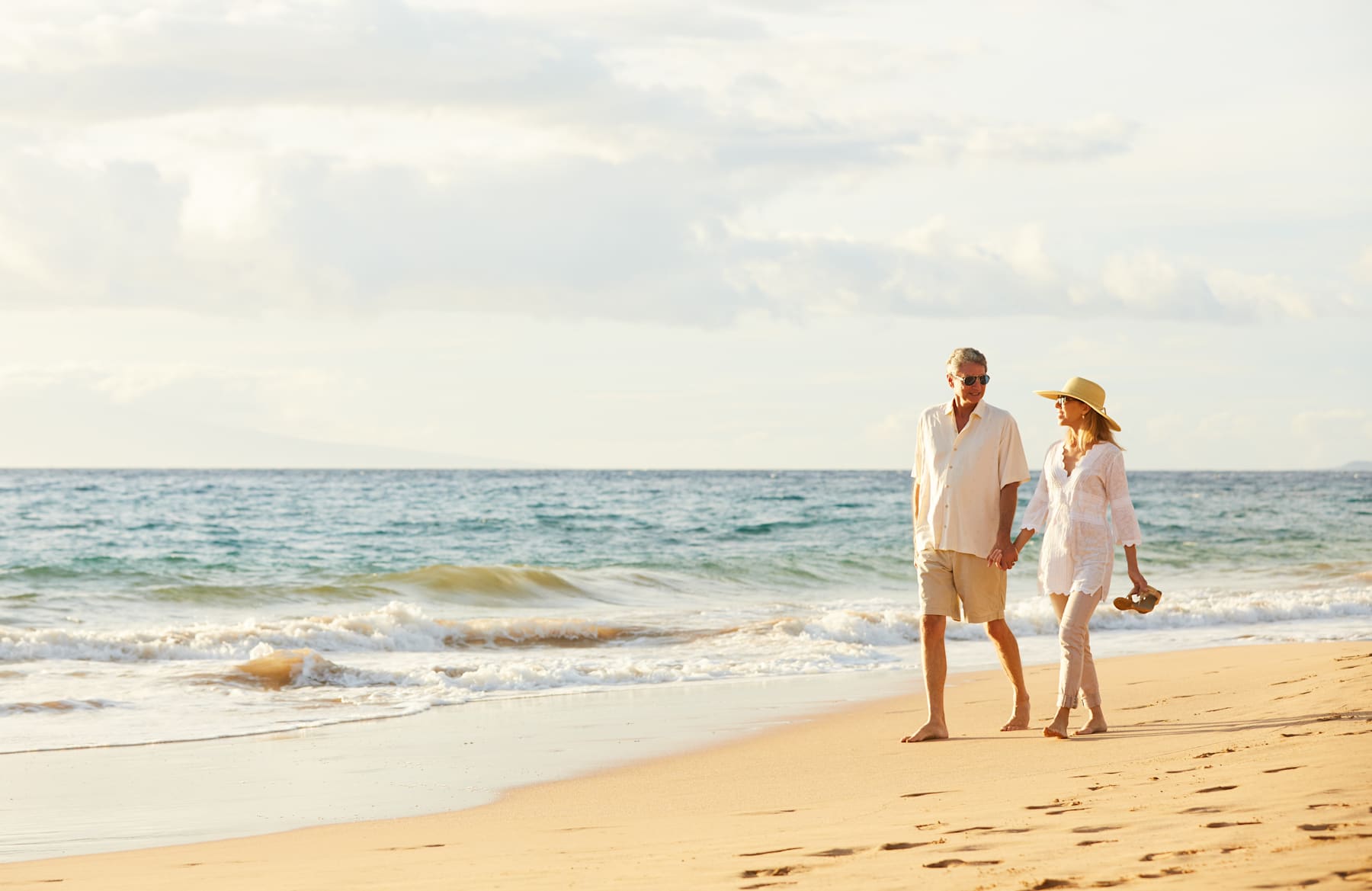 Two people walking together on a sandy beach, with the ocean and cloudy sky in the background.
