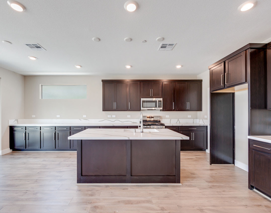 A modern and spacious kitchen with dark wood cabinets, a large island, and stainless steel appliances, set against a light-colored floor and walls.
