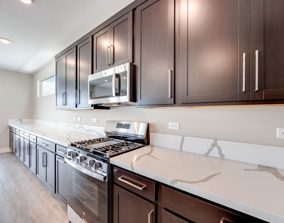 A modern kitchen with dark brown cabinets, a white countertop, and a gas stove in the foreground, set against a bright and airy background.