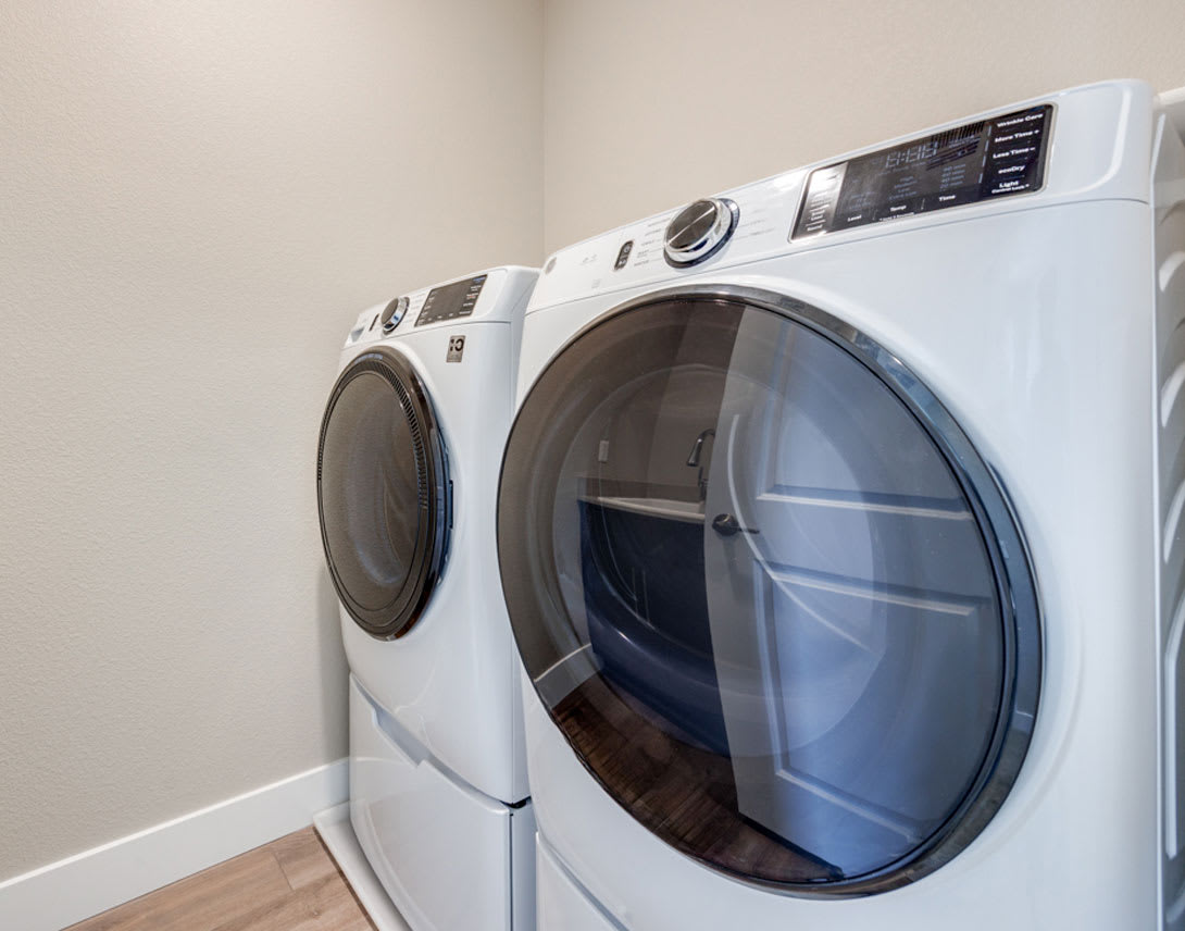 A modern, front-loading washing machine and dryer set against a plain, light-colored wall.