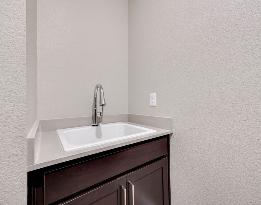 A modern bathroom vanity with a white sink and a dark wooden cabinet against a plain white wall.