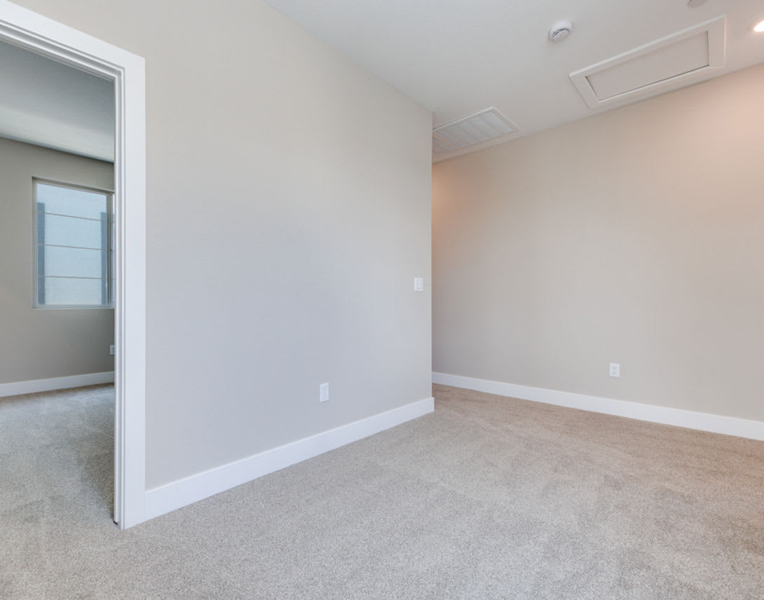 A spacious, well-lit room with white walls, a carpeted floor, and a doorway leading to another area.