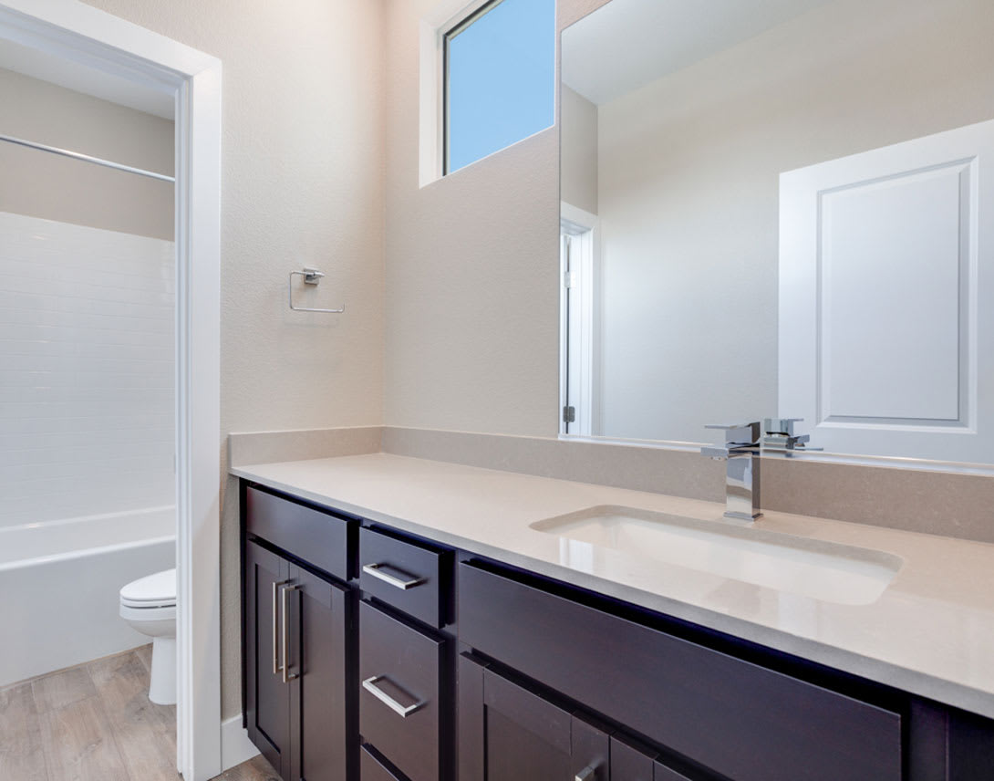 A modern bathroom with a dark wooden vanity, a white countertop, and a large mirror on the wall.