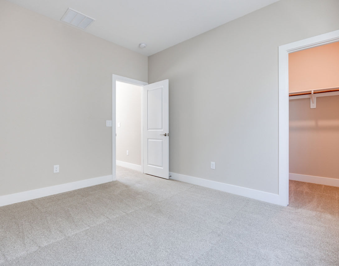 An empty, sparsely furnished room with white walls, a closed door, and a closet visible in the background.