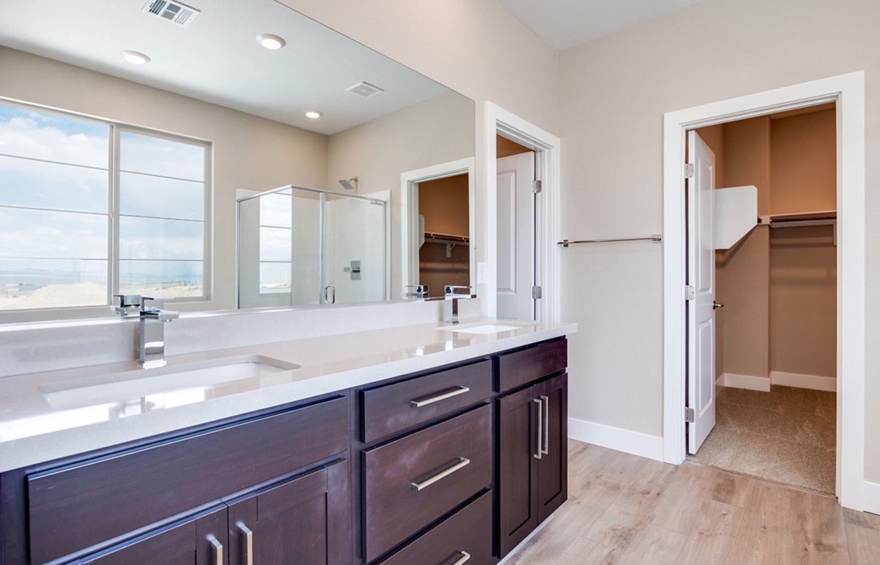 A modern bathroom with a double vanity, a large mirror, and an open closet space in the background, all set against a neutral color palette.