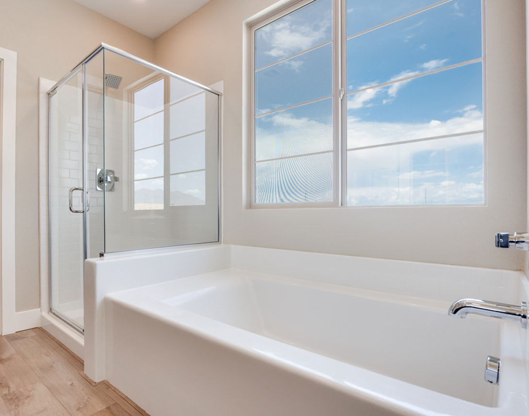 A spacious bathroom with a large window overlooking a scenic view, featuring a white bathtub and a glass-enclosed shower.