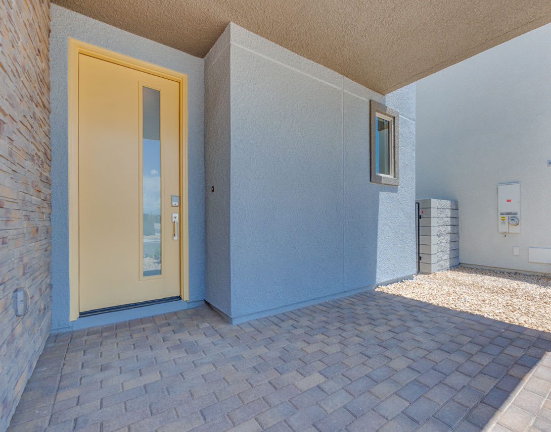 A modern entryway with a yellow door, gray walls, and a paved walkway leading to the entrance.