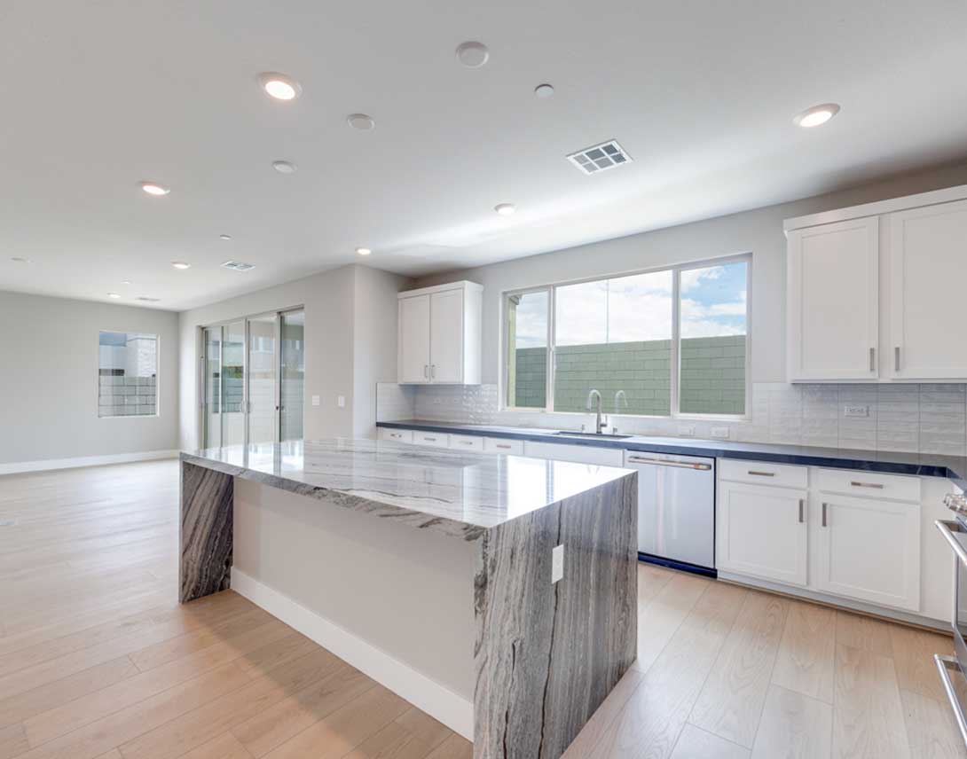 A modern, open-concept kitchen with white cabinets, a large island, and a view of the outdoors through the windows.