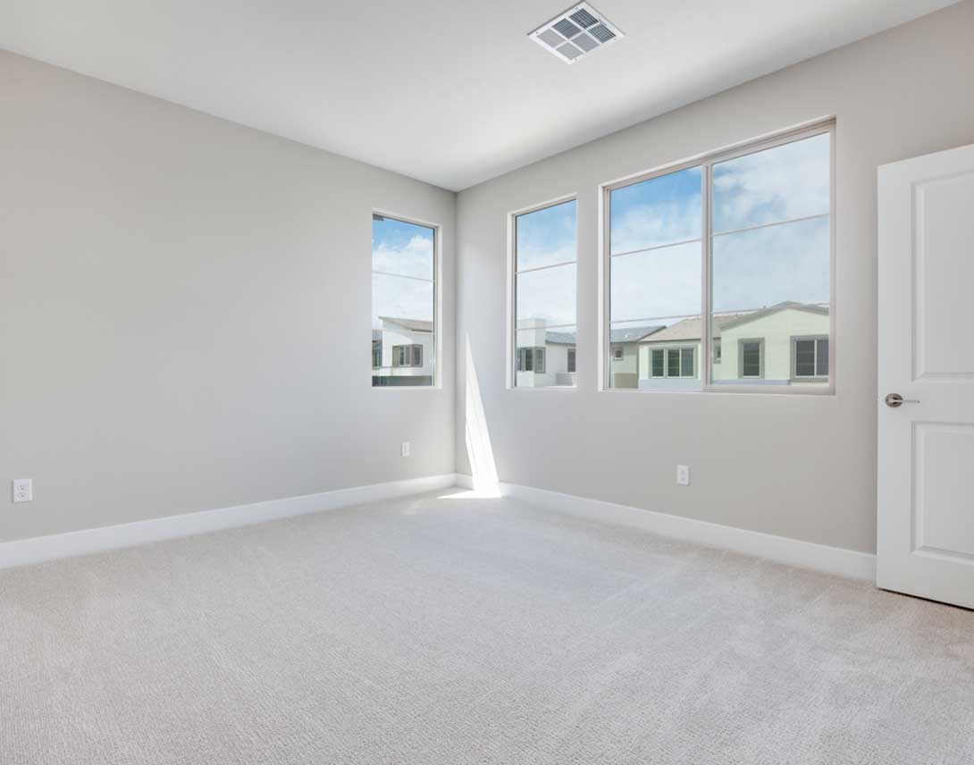 A spacious, bright room with large windows overlooking a residential neighborhood in the background.