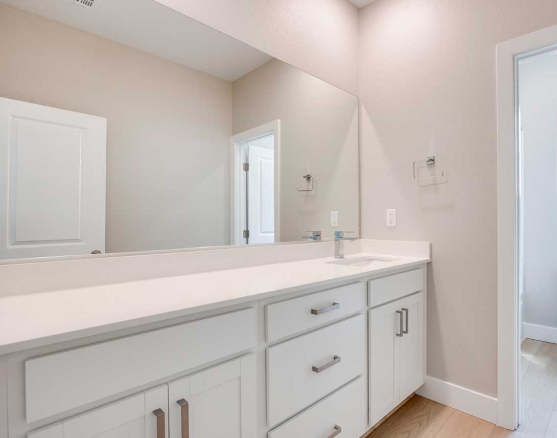 A modern and minimalist bathroom with a white vanity, drawers, and a large mirror taking up the majority of the wall space.