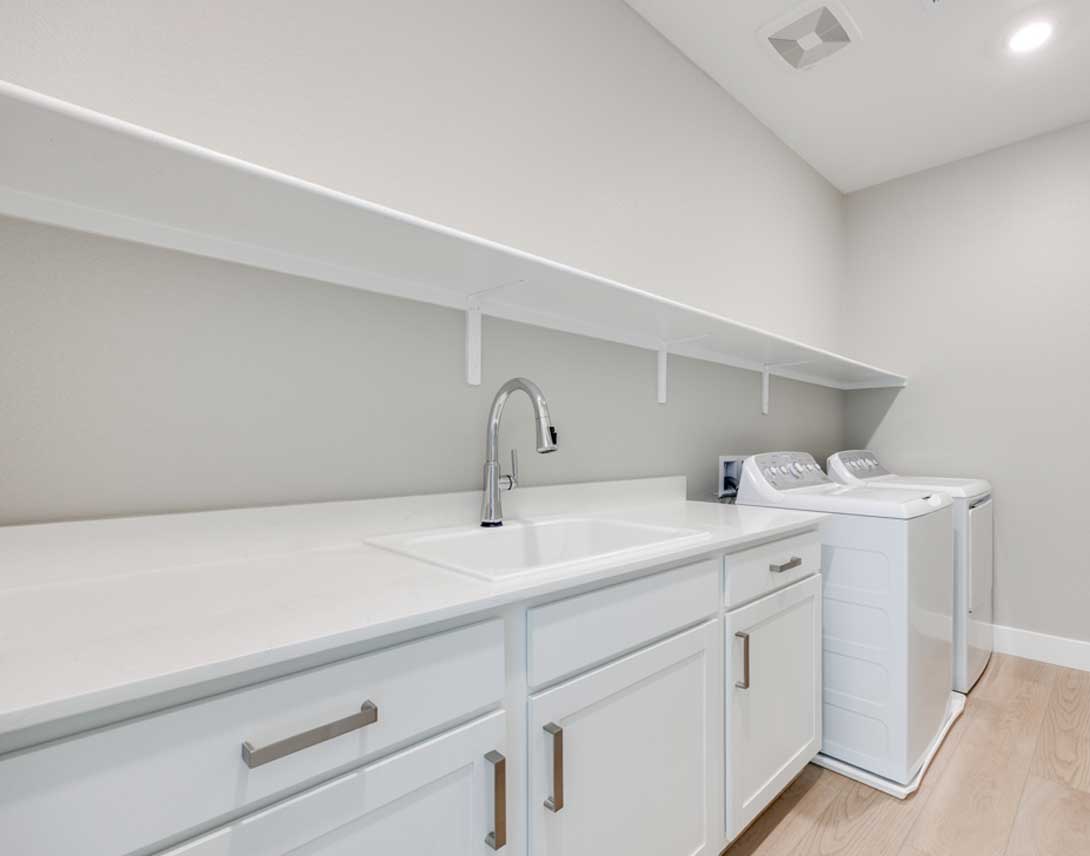A modern, minimalist laundry room with white cabinets, a sink, and a washing machine in the background.