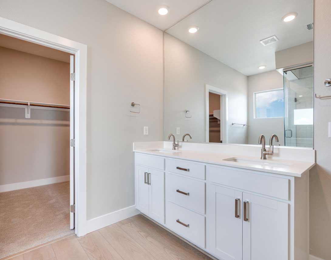 A modern and spacious bathroom with white cabinets, a double vanity, and a glass-enclosed shower area.