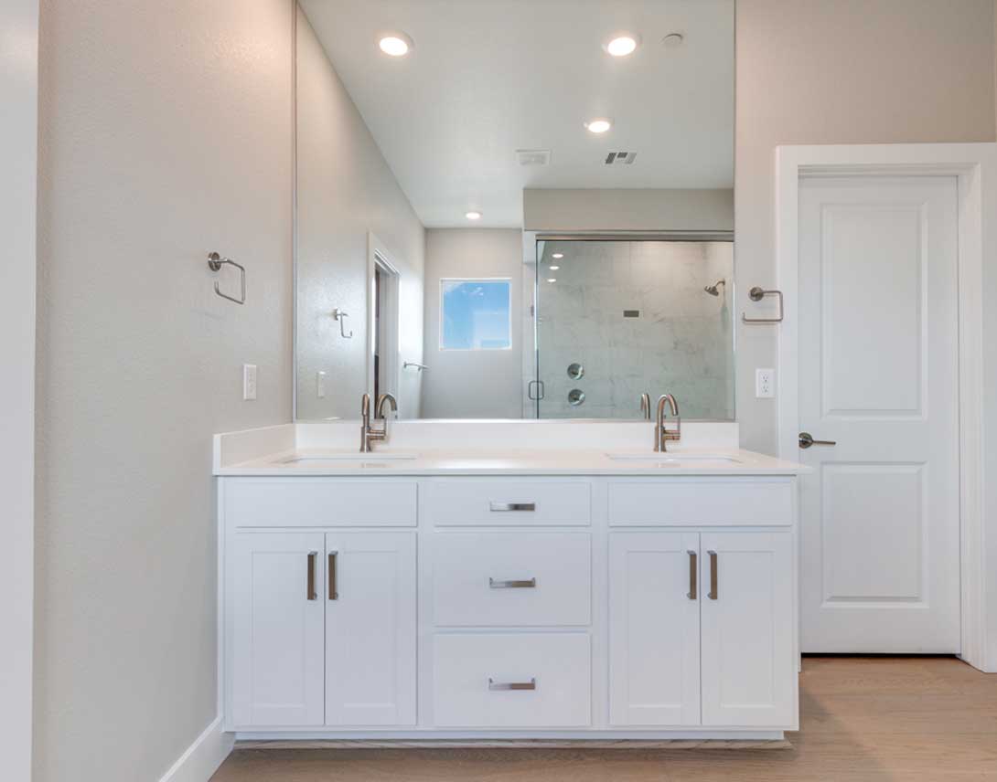 A modern, well-lit bathroom with a white vanity, double sinks, and a glass-enclosed shower in the background.