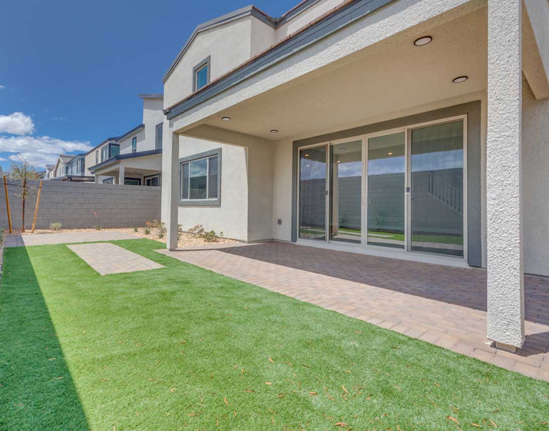 A modern, two-story residential building with a well-manicured lawn and paved walkway in the foreground, set against a clear blue sky.