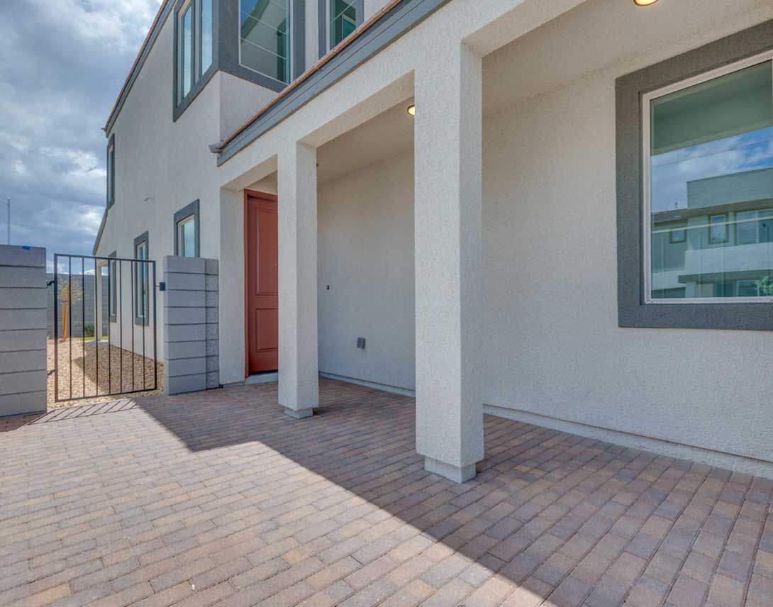 A modern, multi-story building with a red door and a paved walkway leading to it, set against a cloudy sky in the background.